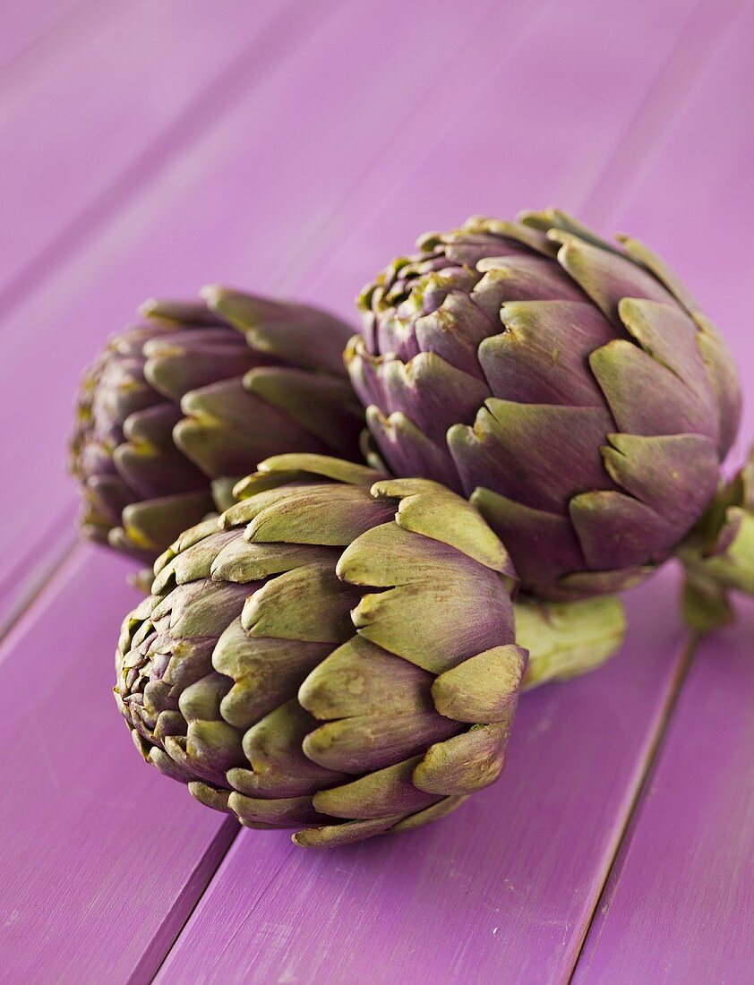 Three Purple Artichokes on Purple Wooden Table