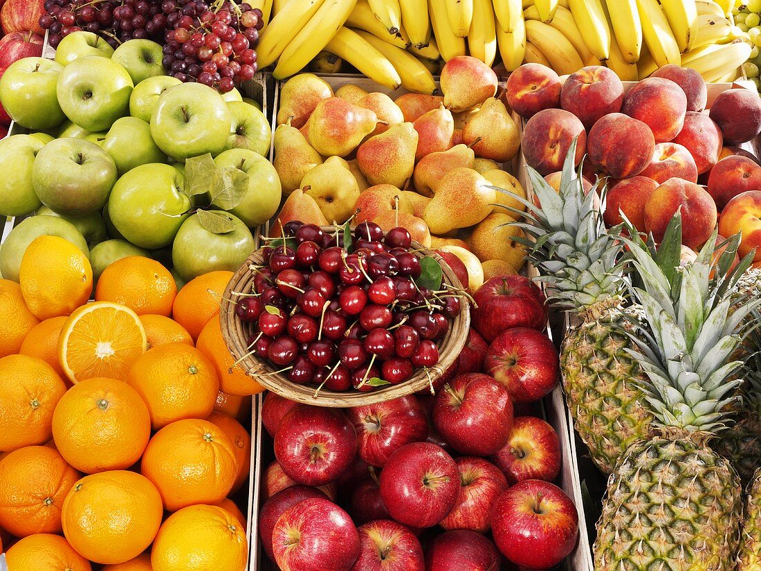 Various types of fruit in crates, cherries on plate at market