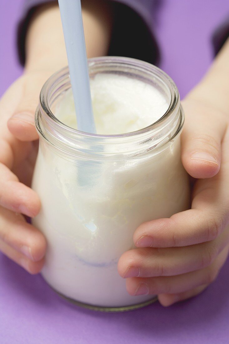 Child's hands holding jar of yoghurt with spoon