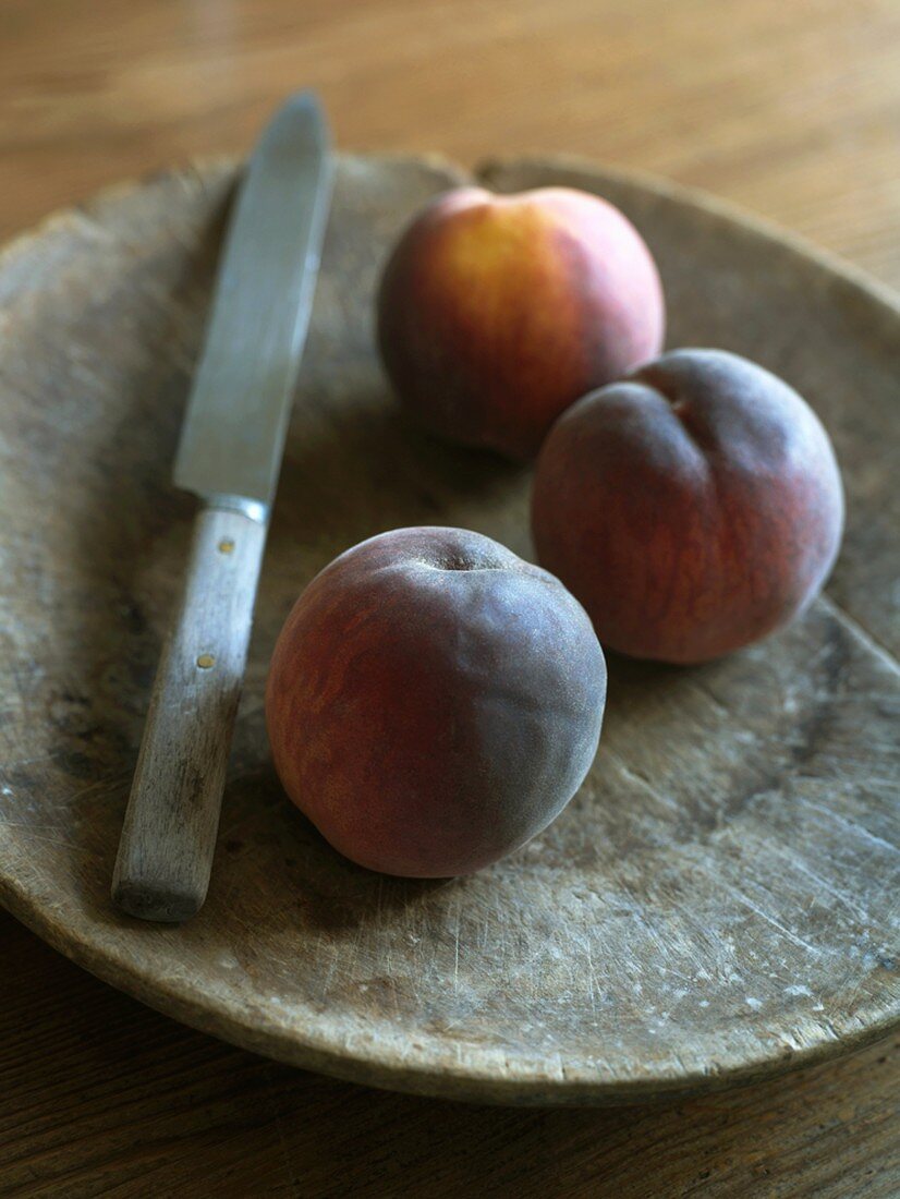 Drei Pfirsiche mit Messer auf einem Holzteller