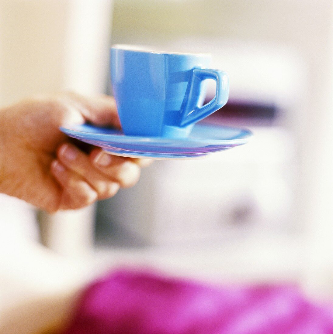 Hand hält eine blaue Kaffeetasse mit Untertasse
