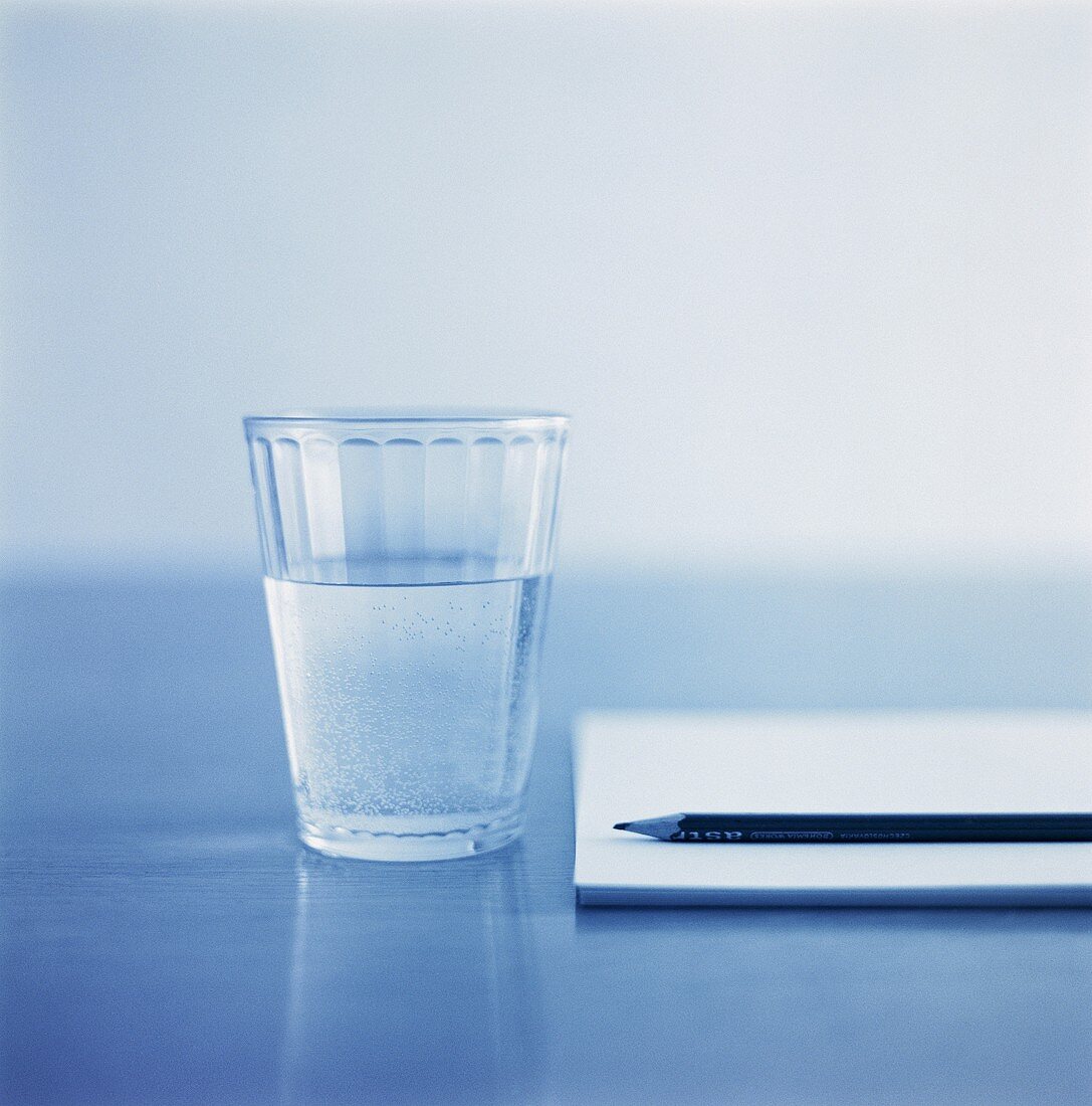 A glass of mineral water beside a notebook and pencil