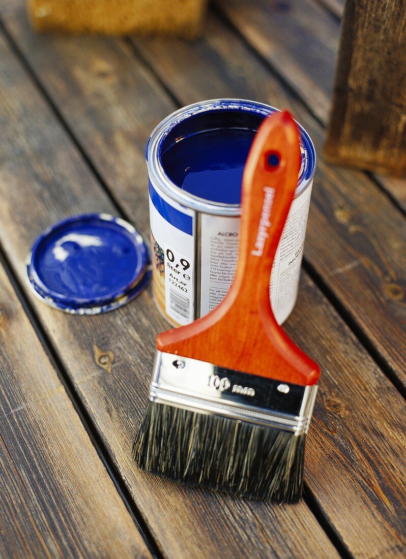 Pot of blue paint and paintbrush on a wooden floor