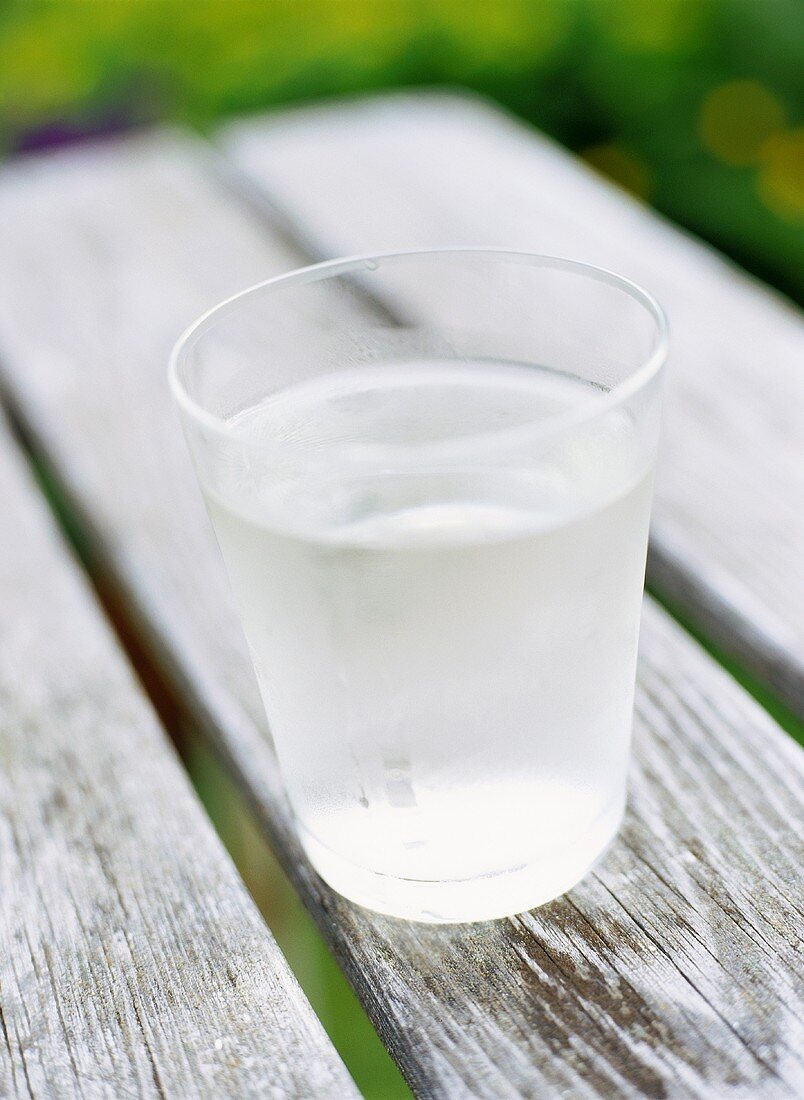 Ein Gals Wasser auf einem Tisch im Freien