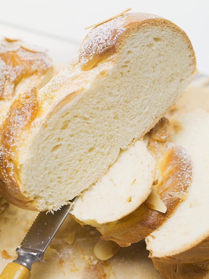 Bread plait with flaked almonds & icing sugar, partly sliced