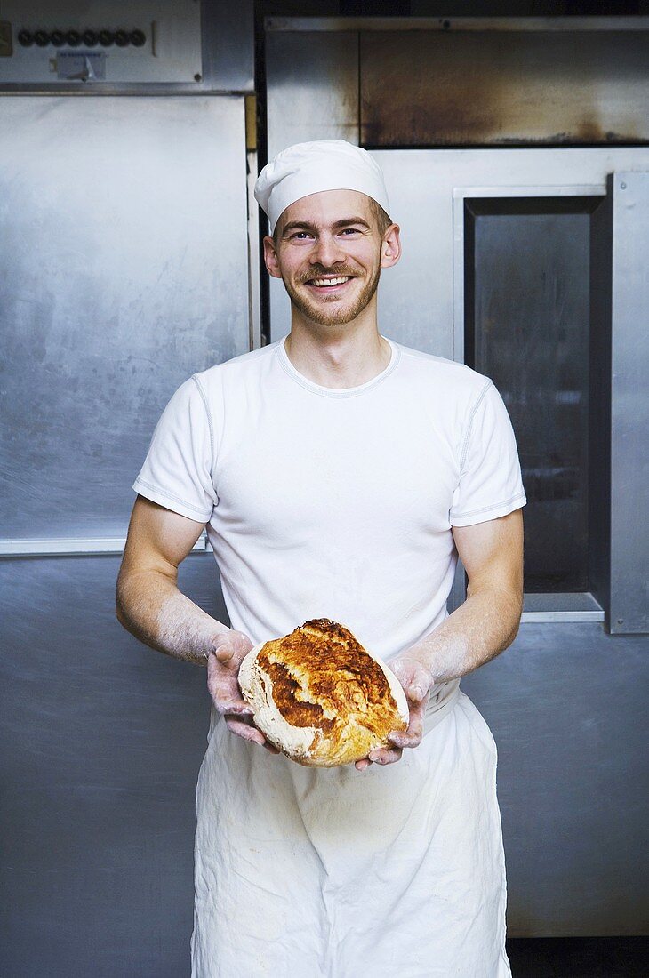Bäcker hält frisch gebackenes Brot in Bäckerei (Schweden)