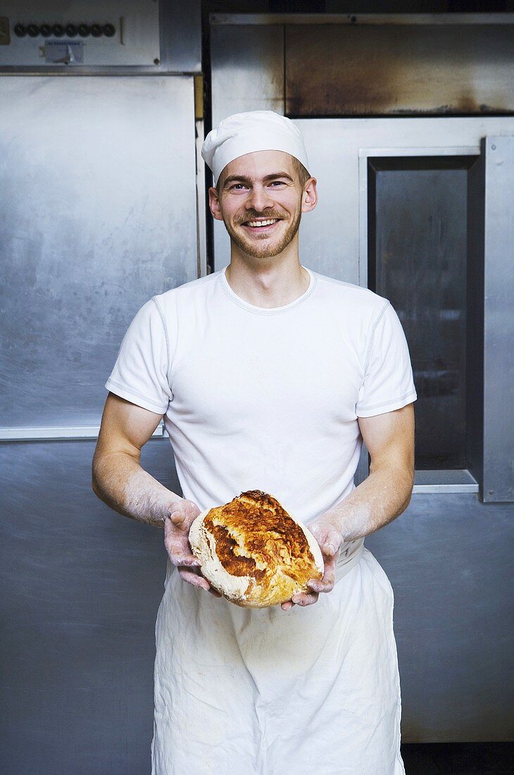 Baker holding freshly baked bread in bakery (Sweden)