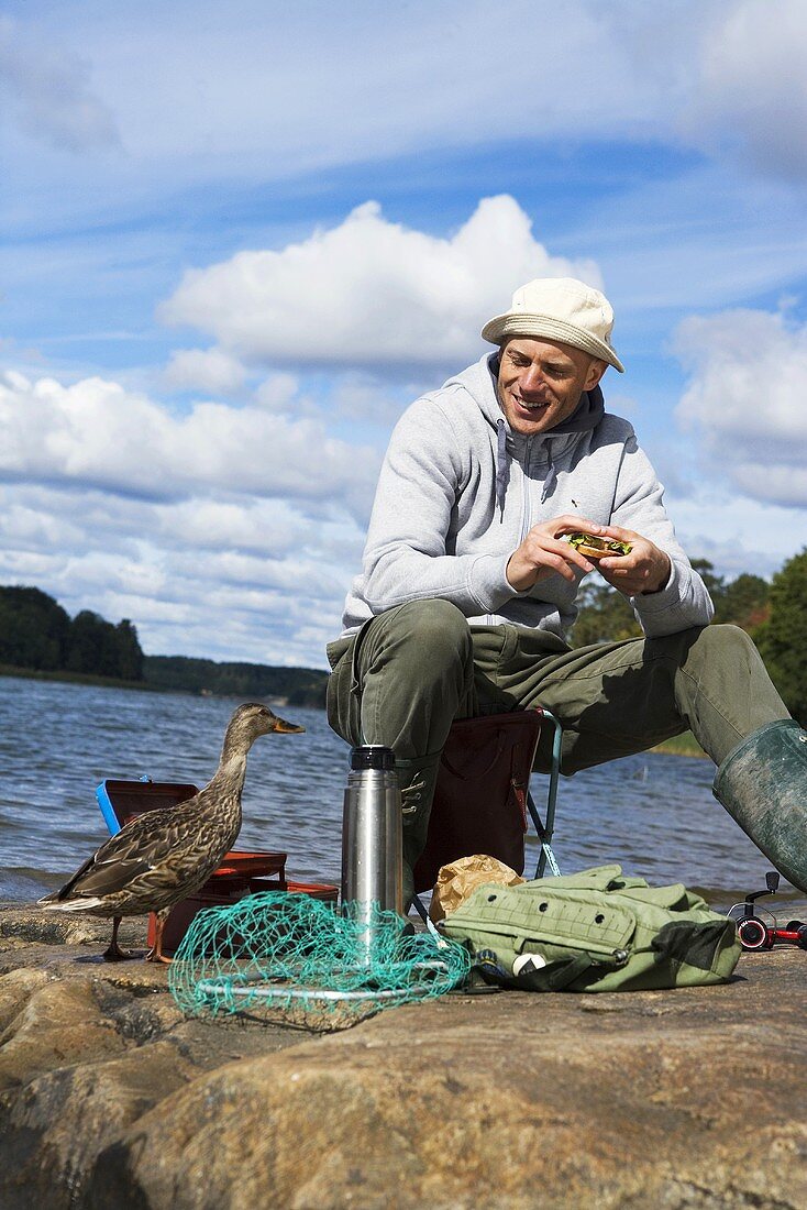 Mann isst Sandwich am Meer (Schweden)