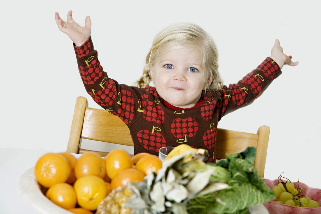 Blond girl sitting in front of fresh fruit and vegetables