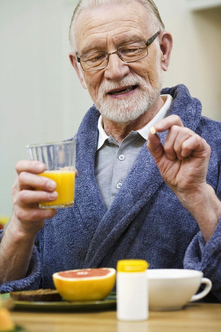 Elderly man taking tablet at breakfast