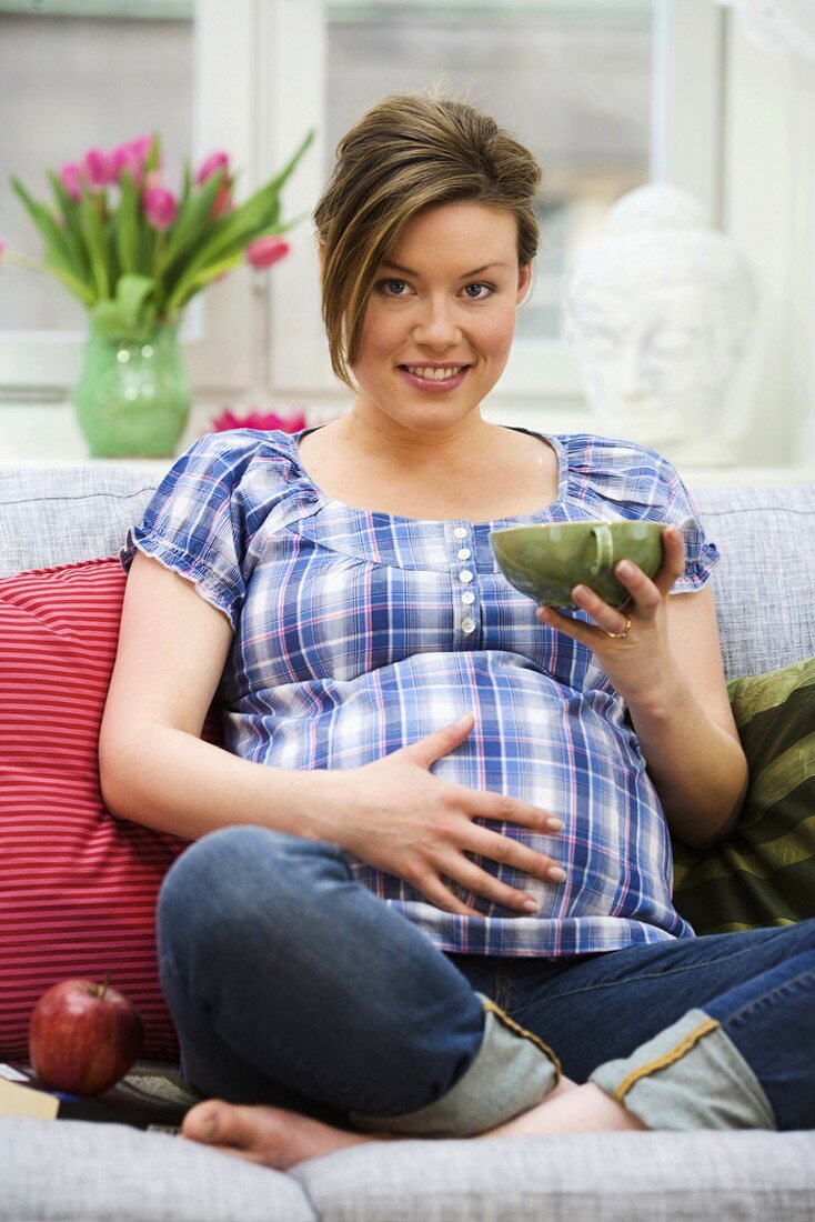 Pregnant woman drinking tea on sofa