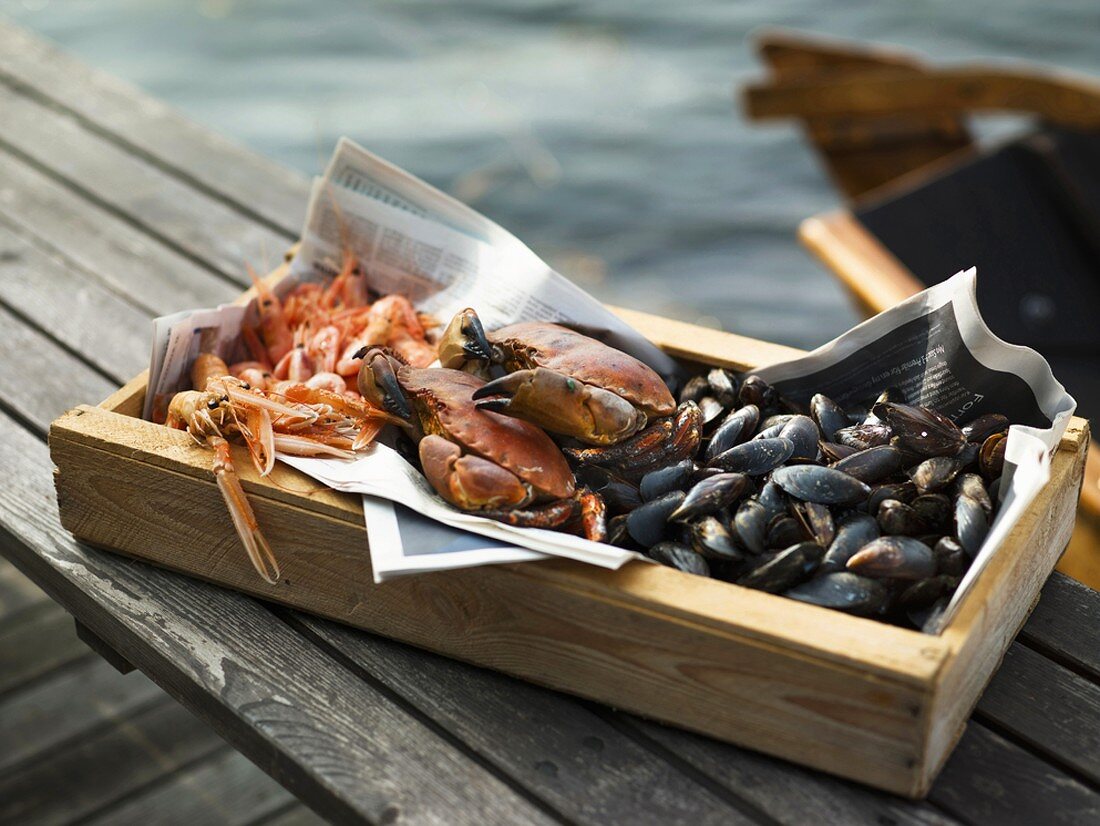 Prawns, crabs and clams in wooden box by sea