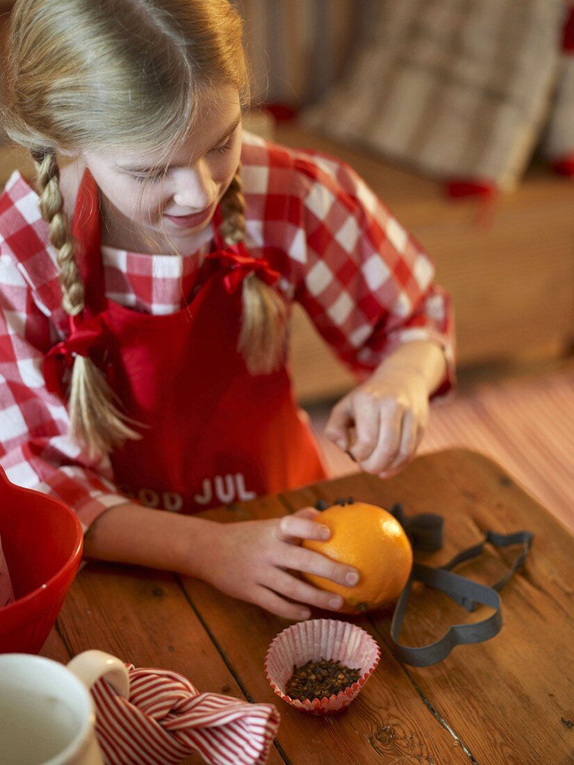 Mädchen steckt Gewürznelken in Orange