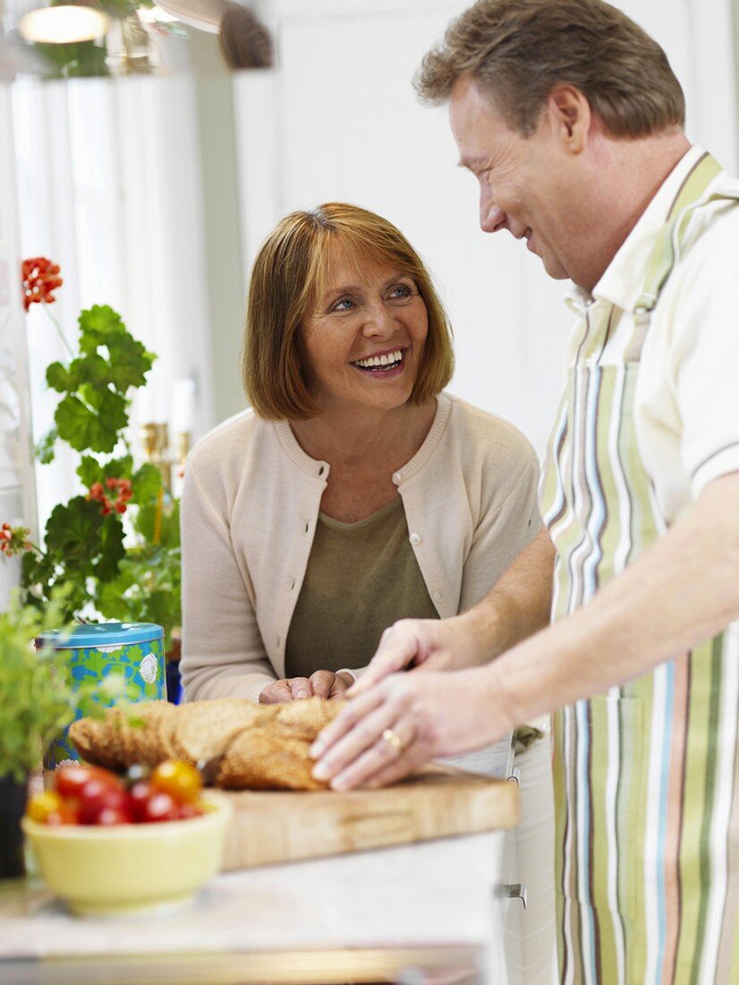 Couple in kitchen, man cutting bread