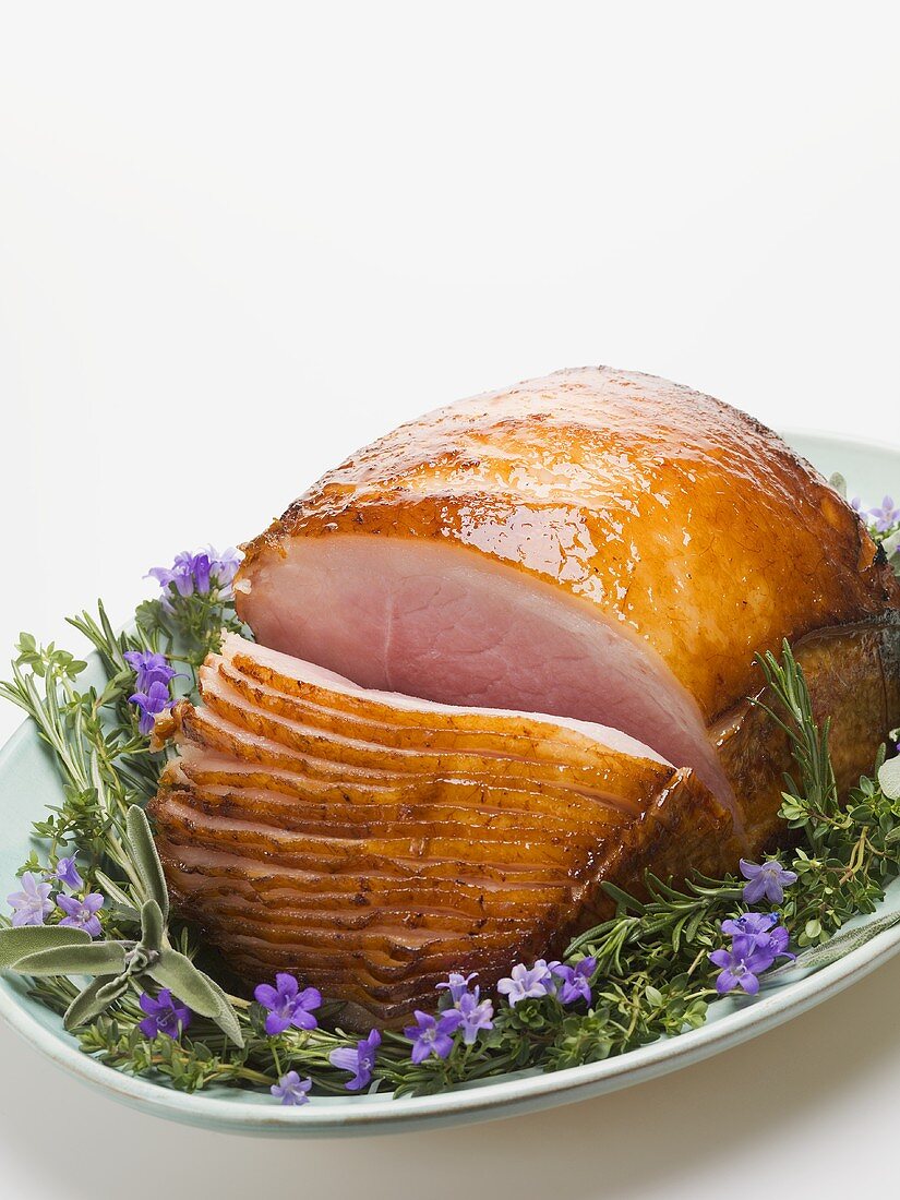Glazed roast ham surrounded by herbs