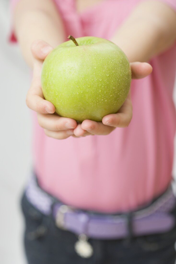 Child holding Granny Smith apple with drops of water