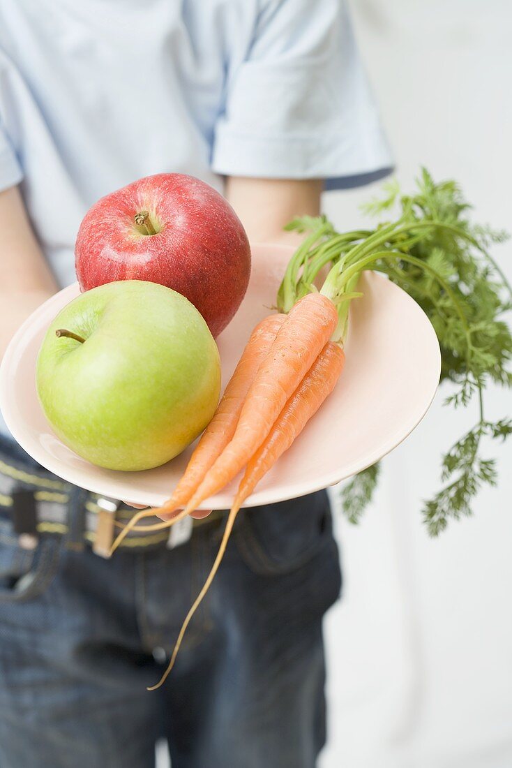 Kind hält Teller mit Äpfeln und Karotten