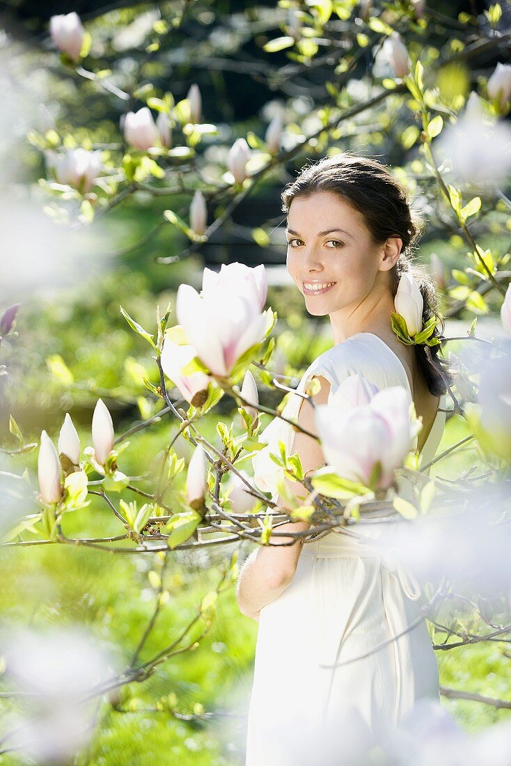 Junge Frau steht am blühenden Magnolienbaum