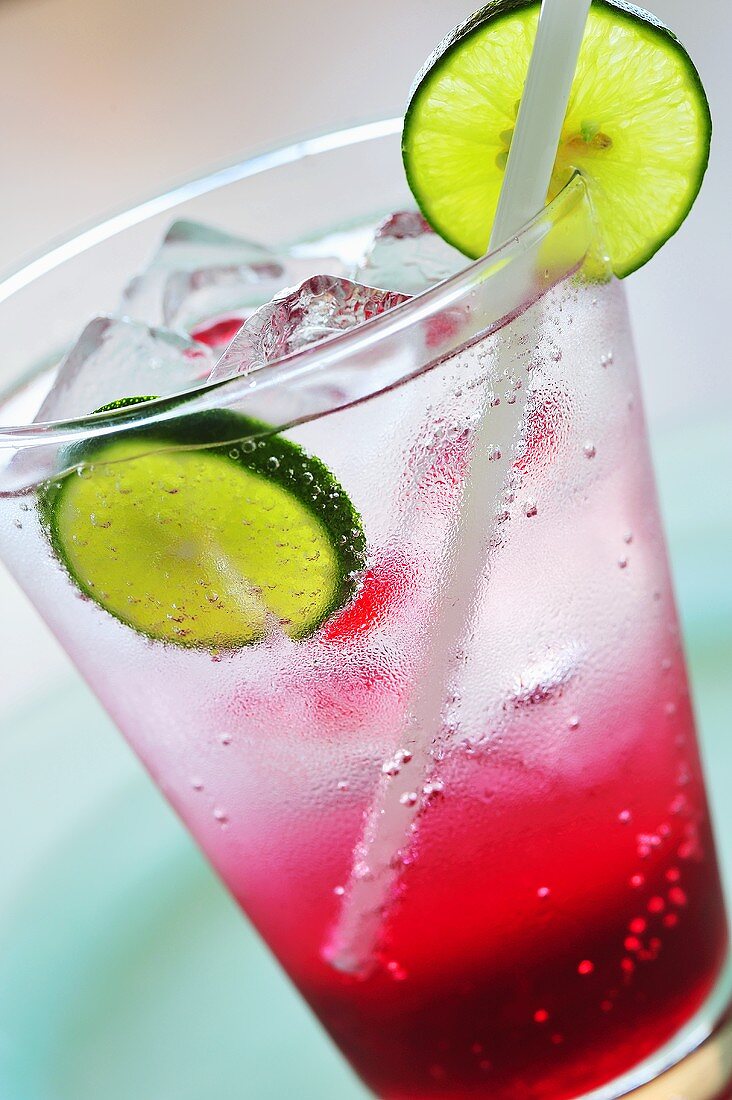A glass of raspberry soda with ice cubes and lime slices