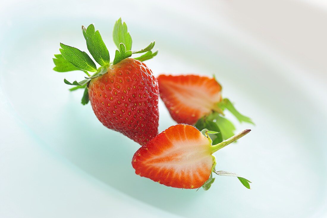 Whole and halved strawberry on a plate