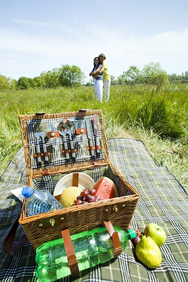 Picnic basket in meadow, young couple in background