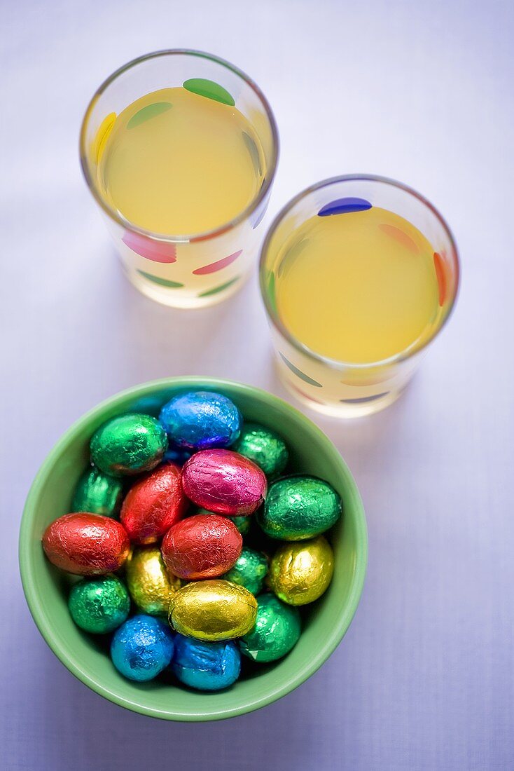 Chocolate eggs in coloured foil and two glasses of juice