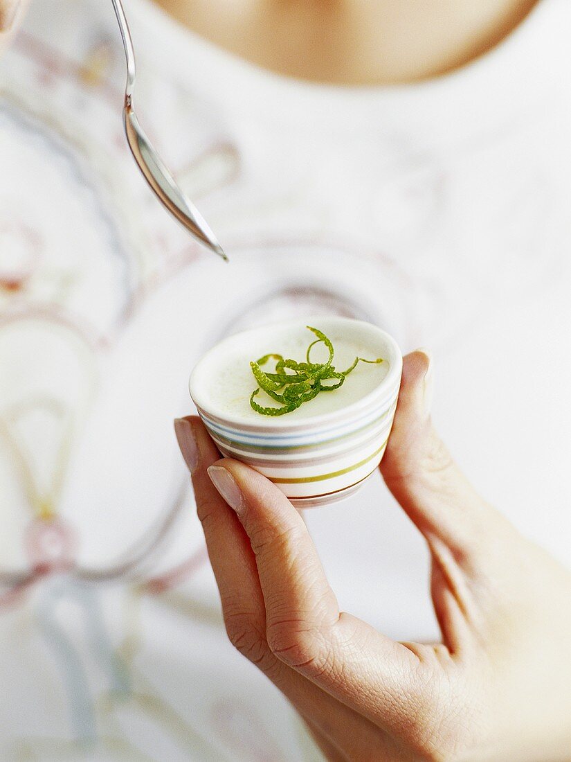 Woman holding small dish of panna cotta with lime zest
