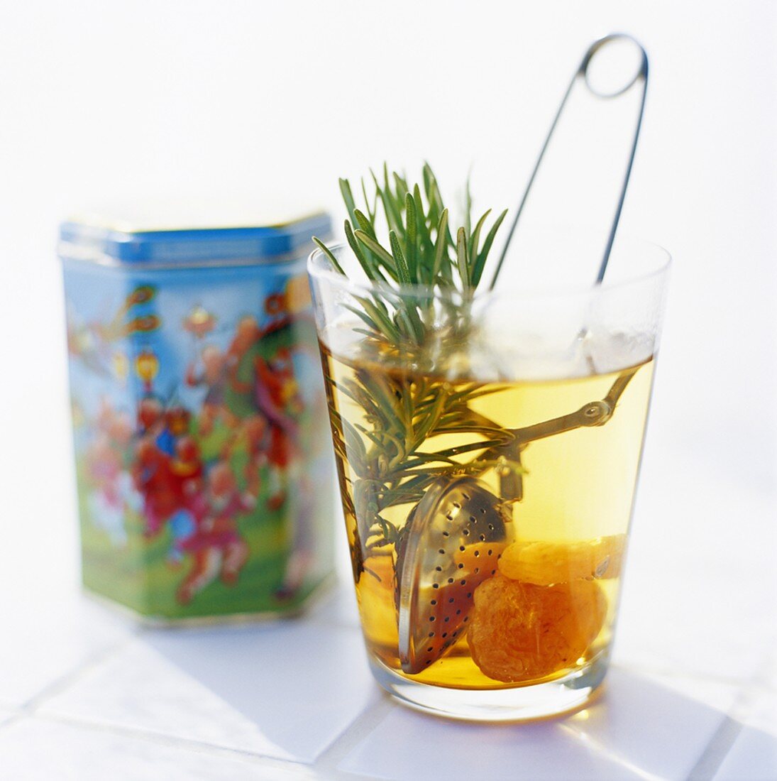 Tea with rosemary and dried fruit in glass, tea tin