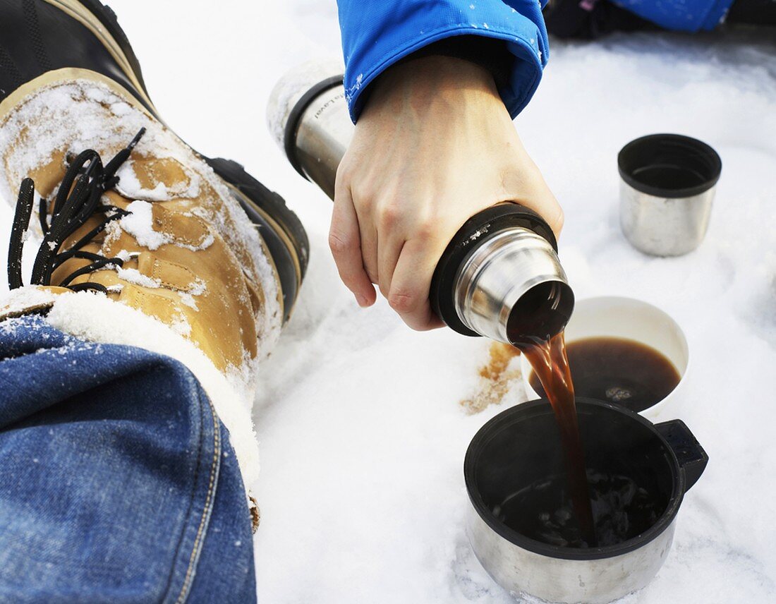Hand pouring hot coffee from Thermos flask into cup