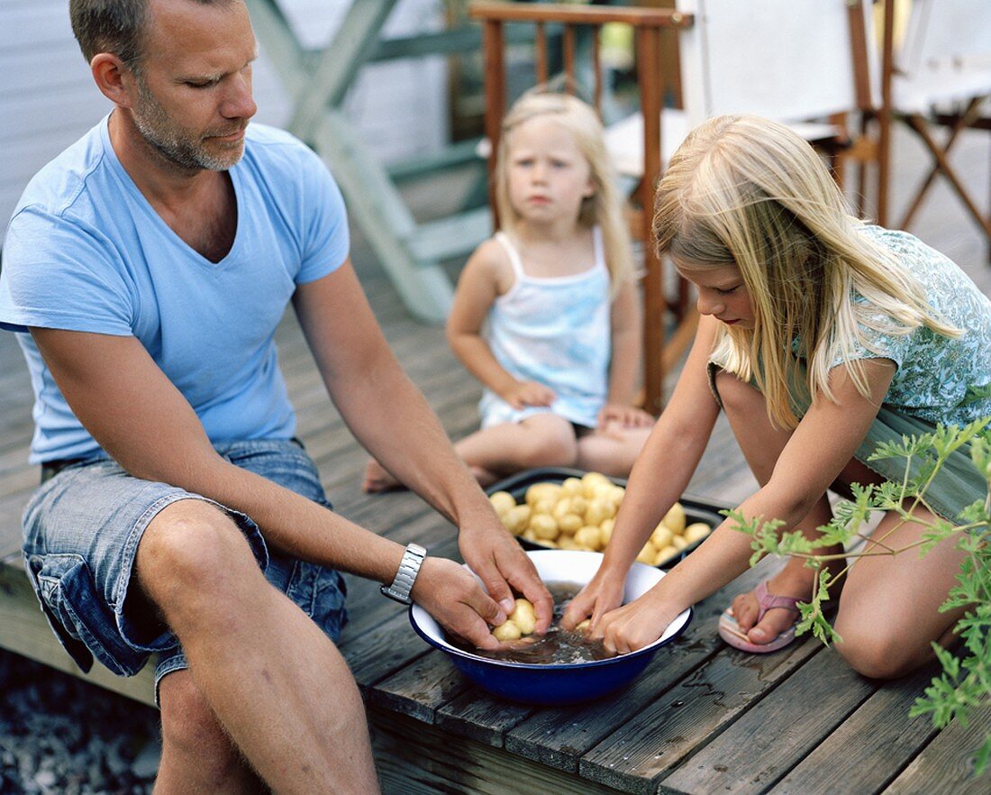 Vater und Töchter schälen Kartoffeln im Freien
