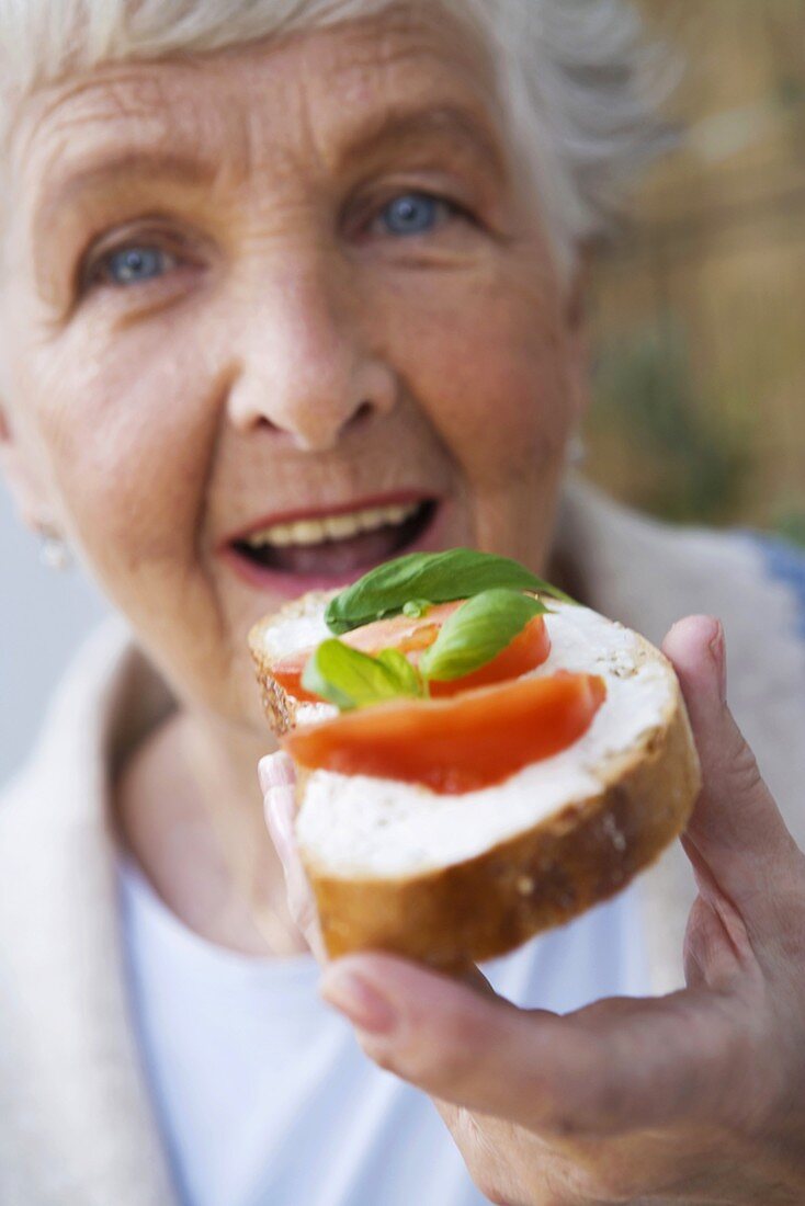 Frau isst Brot mit Frischkäse, Tomaten und Basilikum