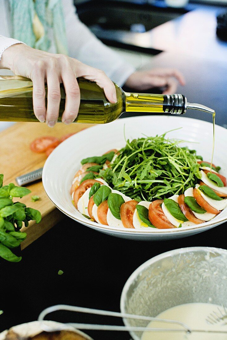 Olivenöl auf Tomaten mit Mozzarella und Basilikum gießen