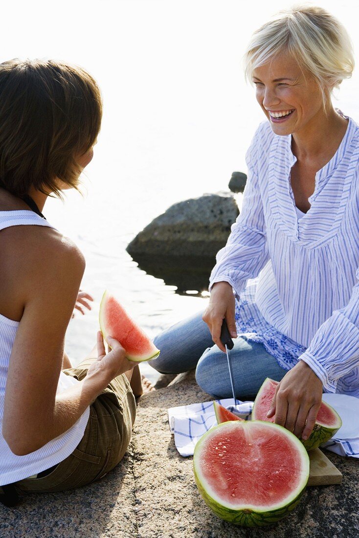 Zwei Frauen essen Wassermelone am Seeufer