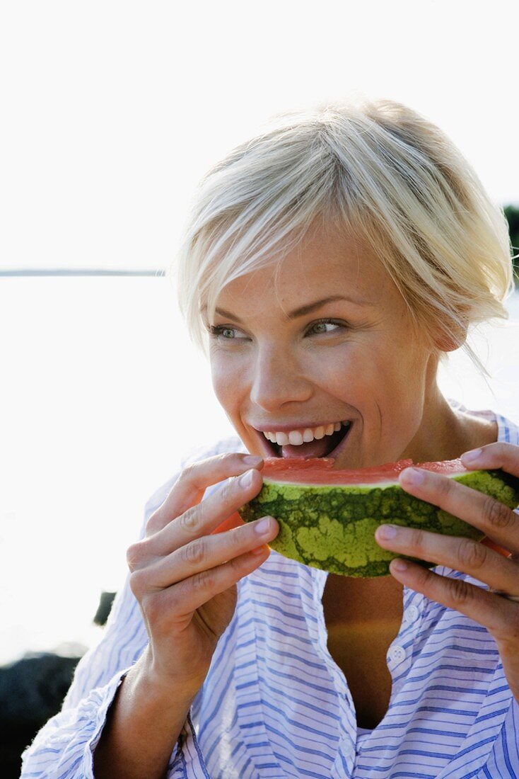 Woman eating watermelon by side of lake