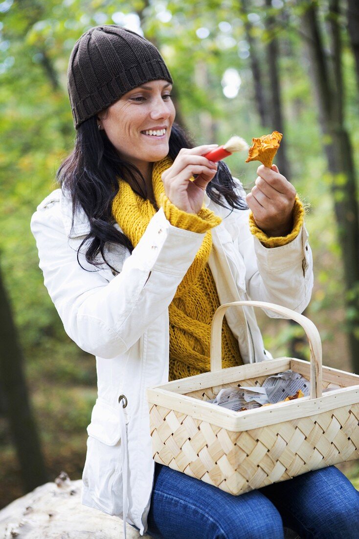 Woman cleaning chanterelle with brush in wood