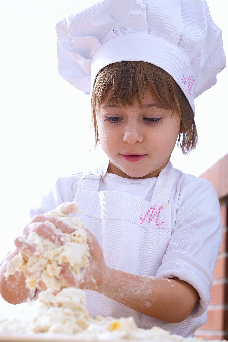 Little girl in chef's hat kneading dough