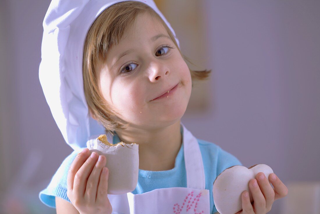 Kleines Mädchen mit Kochhaube isst herzförmige Lebkuchen