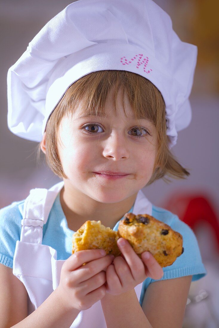 Little girl in chef's hat holding raisin biscuits