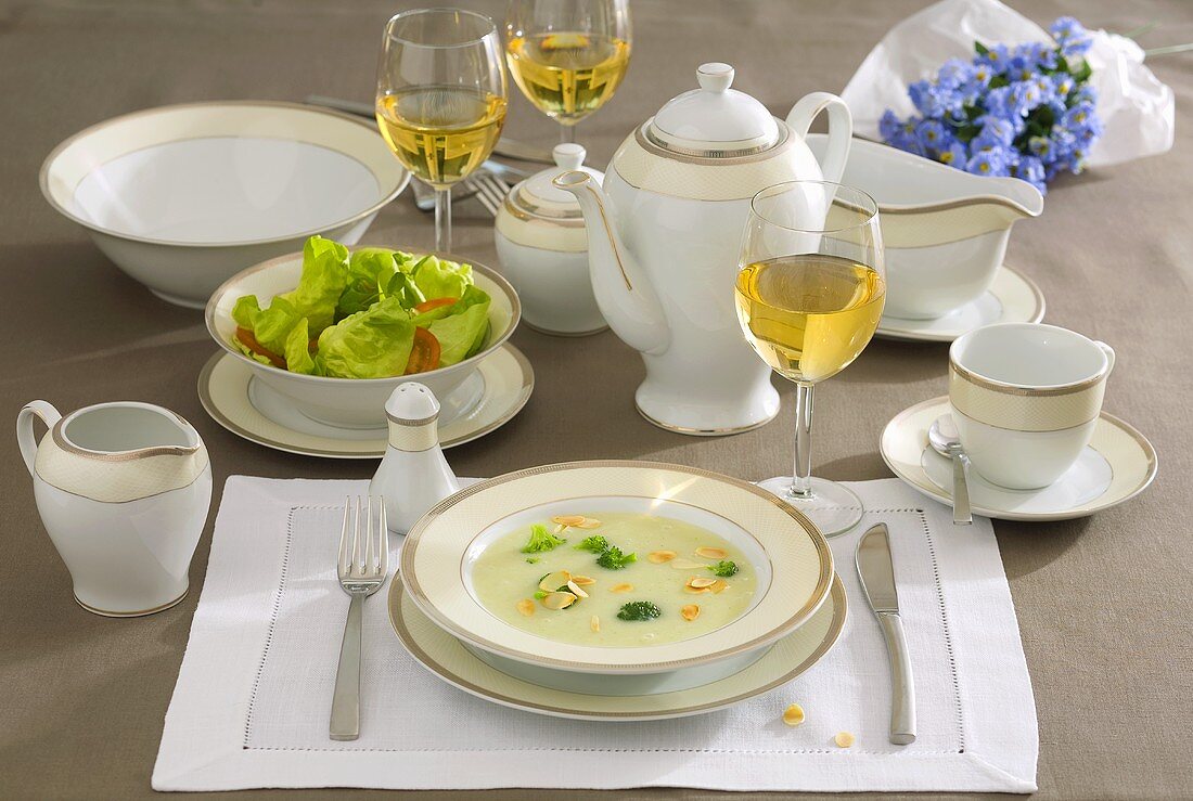 Place-setting with broccoli soup, salad and white wine
