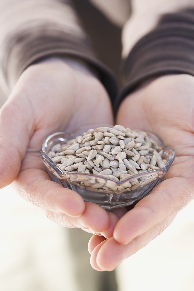 Hands holding glass dish of sunflower seeds