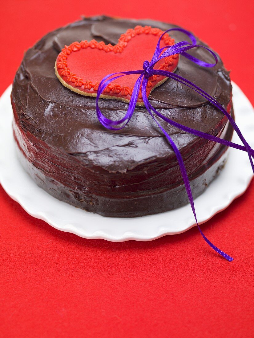 Chocolate cake with red heart-shaped biscuit and bow