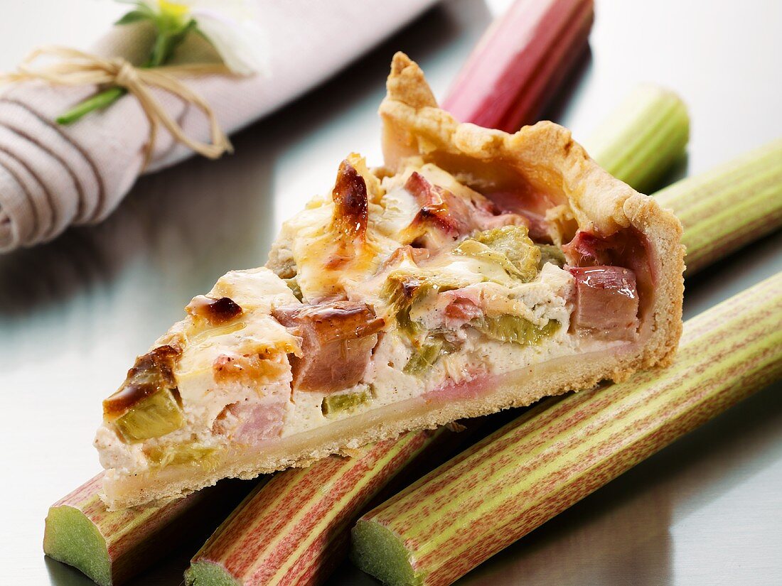 Piece of rhubarb tart on fresh sticks of rhubarb