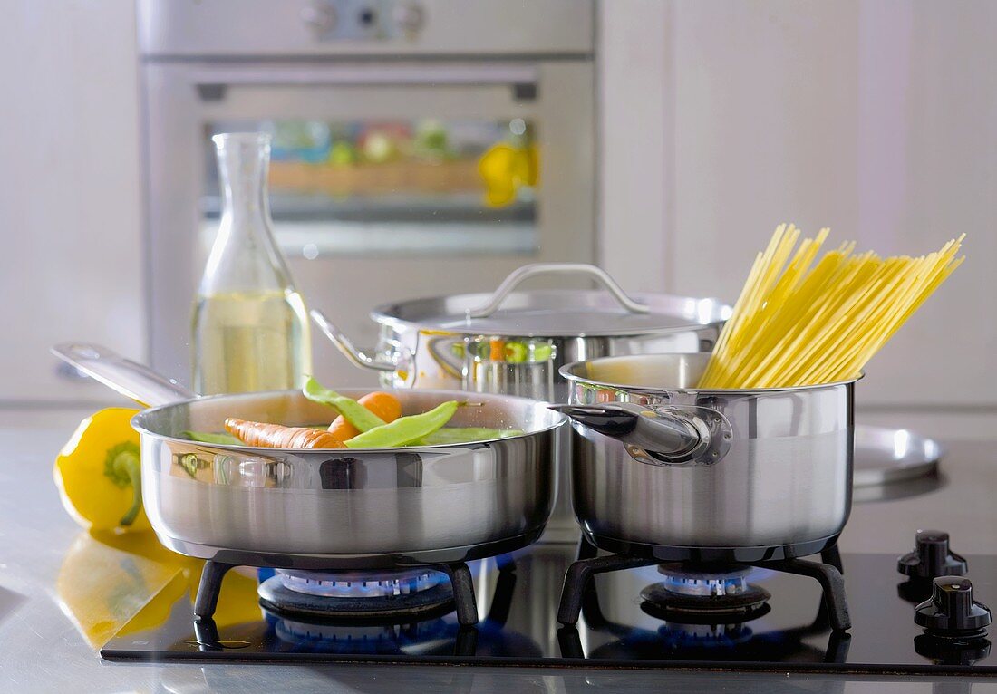 Vegetables and spaghetti in pans on a gas cooker