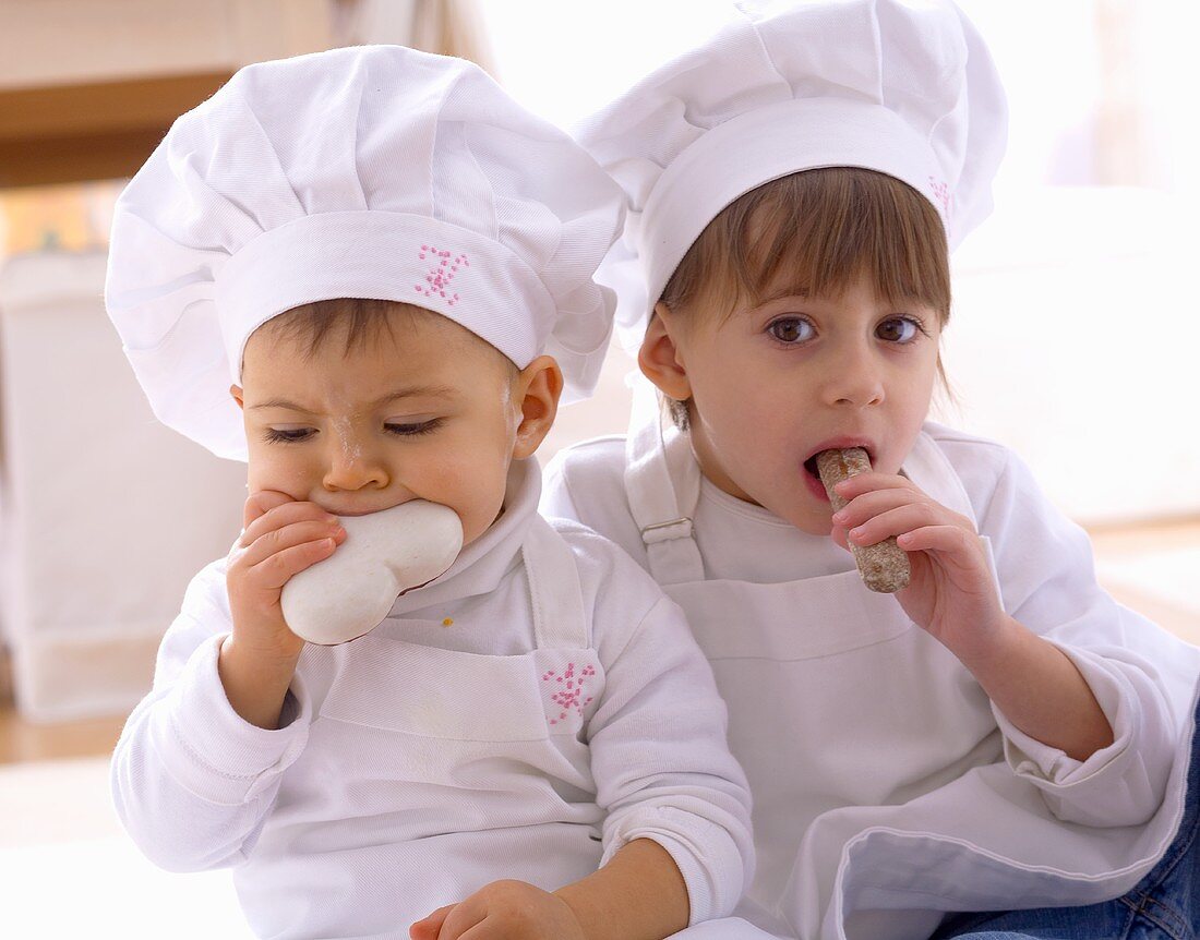 Two girls in chefs' hats eating biscuits
