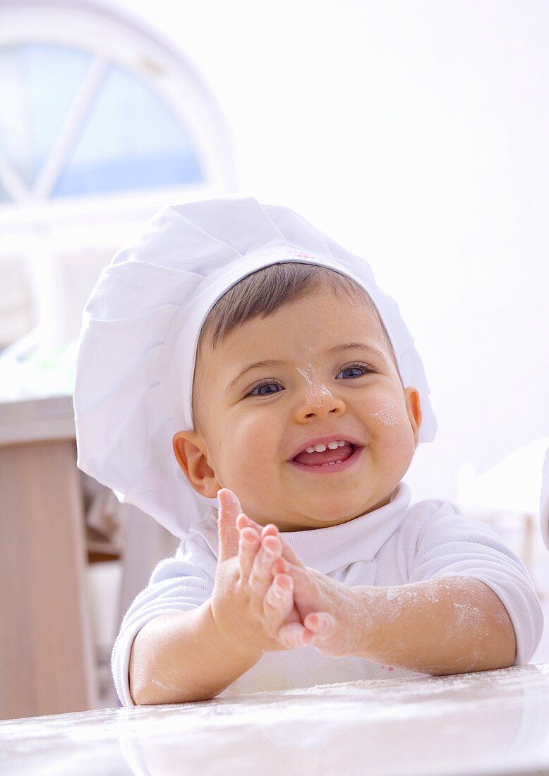 Kleines Mädchen mit Kochmütze und bemehlten Händen