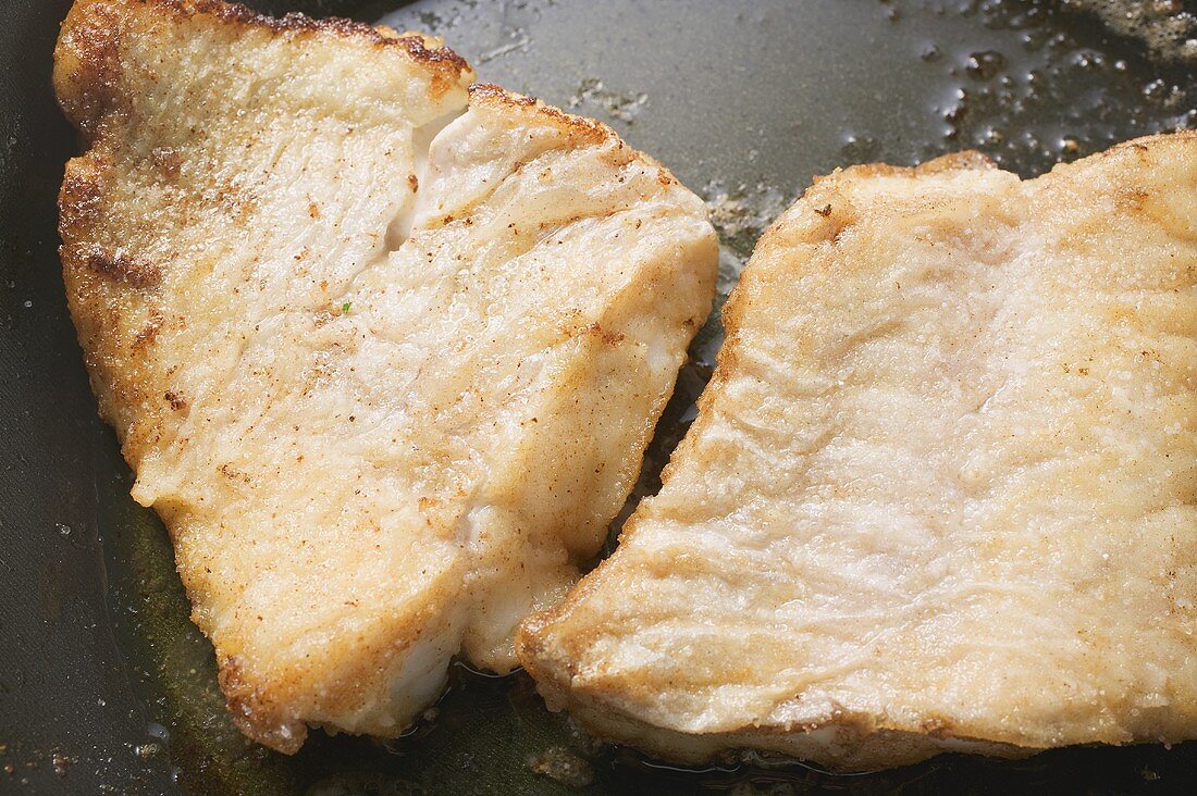 Two fried fish fillets in frying pan (close-up)