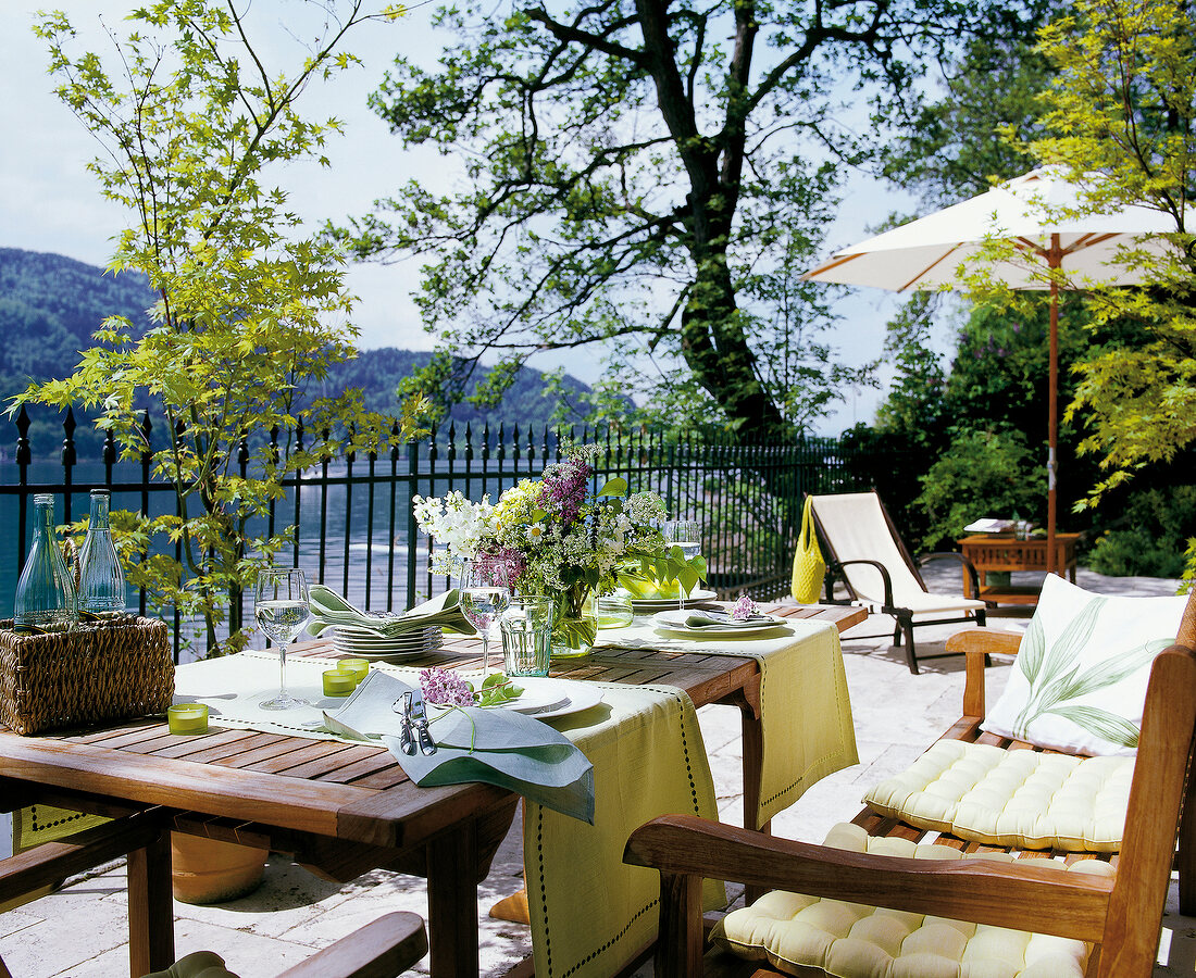 Laid table with flower vase and wooden sofa on terrace