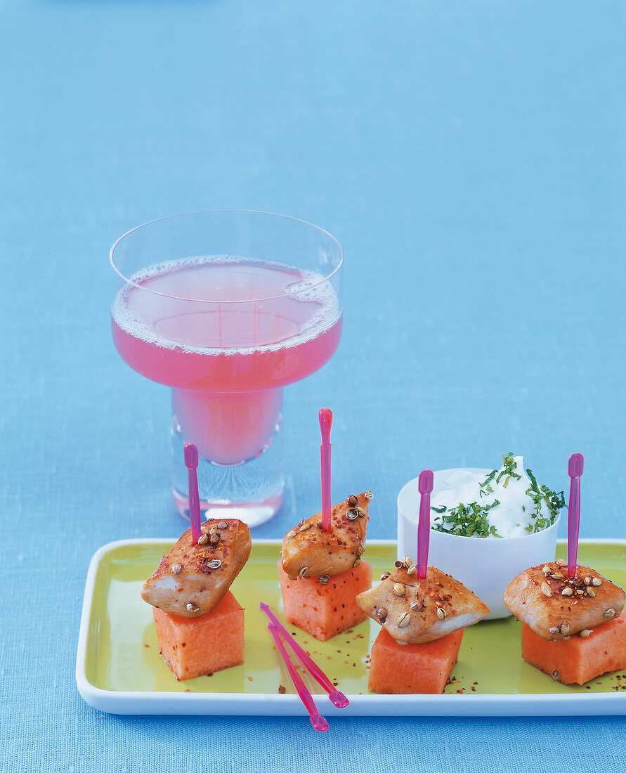Chicken and melon slices in skewers on plate with melon drink in martini glass