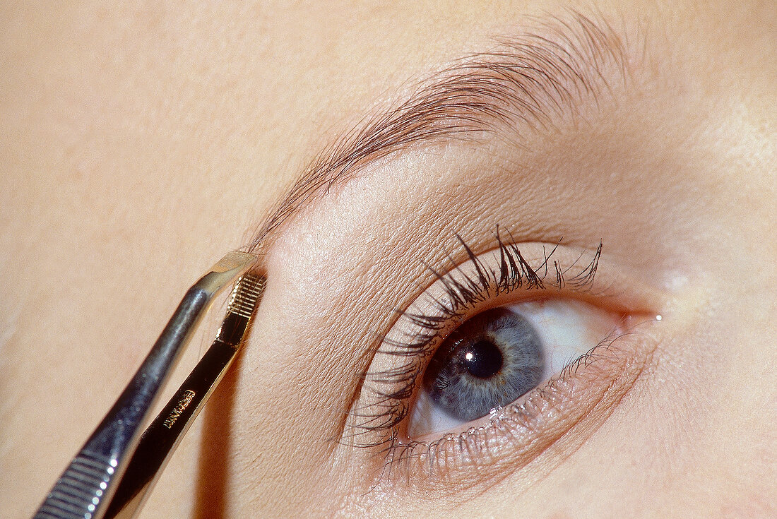 Close-up of gray eyed woman plucking her eyebrows