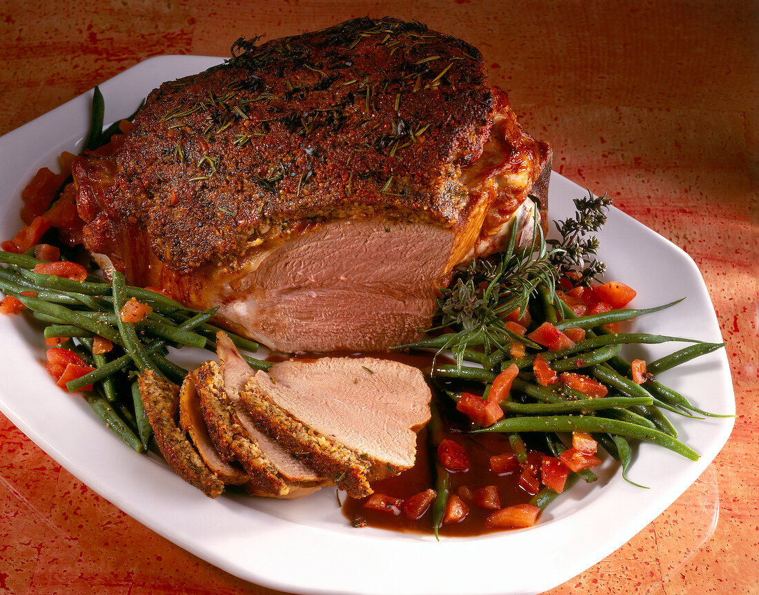 Leg of lamb with mustard crust, baked beans and tomatoes in serving dish
